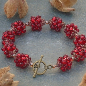 May include: A red beaded bracelet with a gold clasp. The beads are clustered together to form small flower shapes.