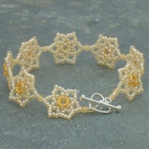 May include: A delicate bracelet made of small, white beads, arranged in a flower pattern. The bracelet has a silver clasp.