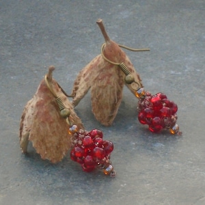 May include: A pair of earrings with a dried leaf design and red glass beads. The earrings are made with bronze-colored metal.