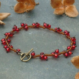 May include: A red beaded bracelet with a brass toggle clasp. The beads are arranged in a cluster pattern, resembling a garland of berries.