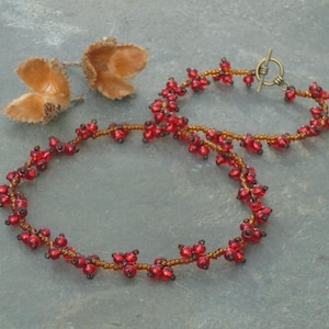 Op de afbeelding: Een rode en bruine kralenketting met een schuifsluiting. De ketting is gemaakt van kleine, ronde kralen die in een delicaat patroon aan elkaar geregen zijn.