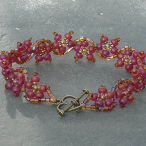 May include: A beaded bracelet with a floral design in shades of red and gold. The bracelet has a clasp closure.