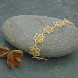 May include: A delicate beaded bracelet with gold-toned flower accents. The bracelet is made of small white beads and features a repeating pattern of flower shapes.