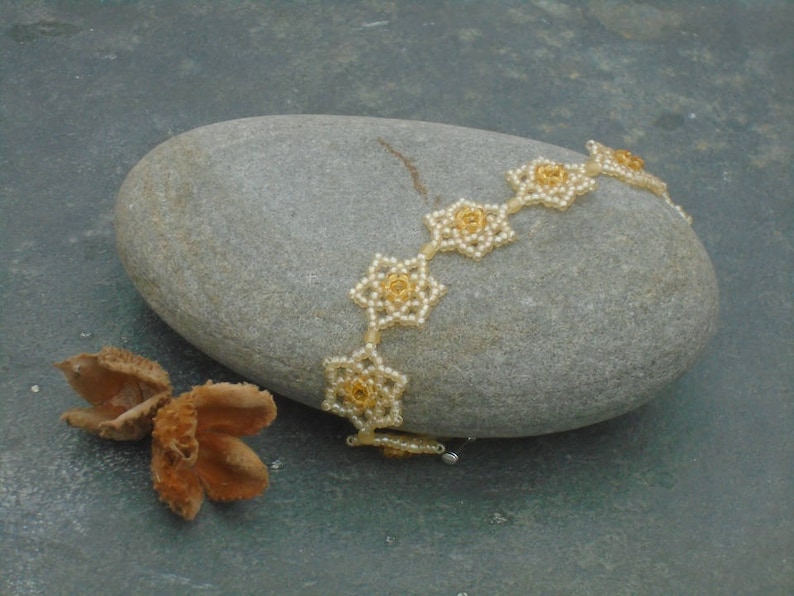 May include: A delicate beaded bracelet with gold-toned flower accents. The bracelet is made of small white beads and features a repeating pattern of flower shapes.