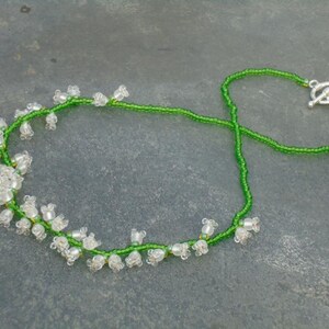 May include: A delicate necklace made with green and white beads, featuring a lily of the valley design. The necklace has a silver toggle clasp.