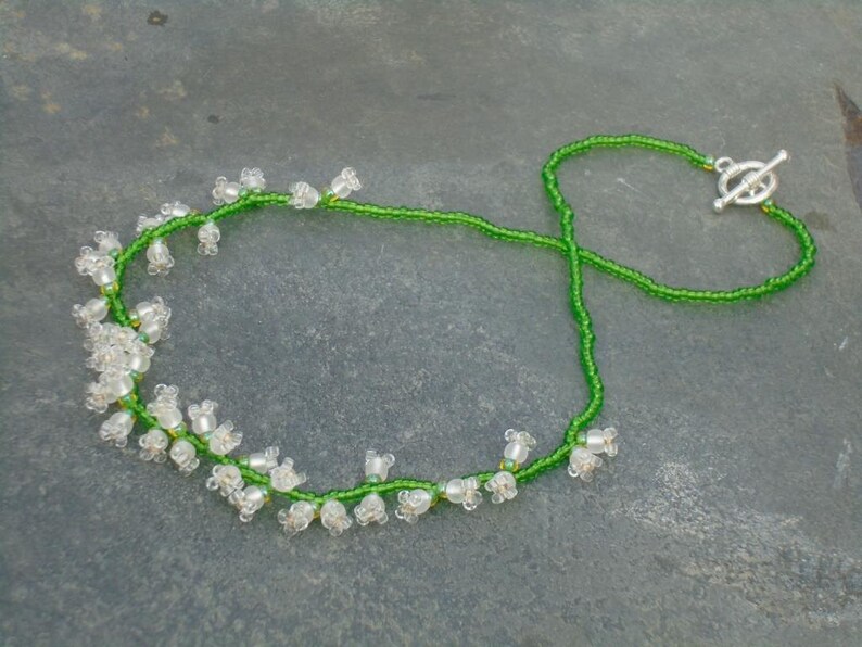 May include: A delicate necklace made with green and white beads, featuring a lily of the valley design. The necklace has a silver toggle clasp.