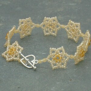 May include: A delicate bracelet made of small, white beads, arranged in a flower pattern. The bracelet has a silver clasp.