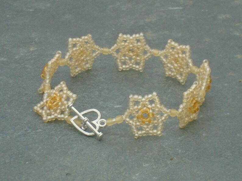 May include: A delicate bracelet made of small, white beads, arranged in a flower pattern. The bracelet has a silver clasp.