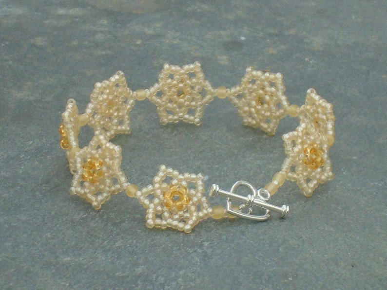 May include: A delicate bracelet made of small, white beads, arranged in a flower pattern. The bracelet has a silver clasp.