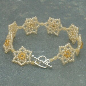 May include: A delicate bracelet made of white and gold beads, featuring a repeating flower design. The bracelet has a silver clasp.