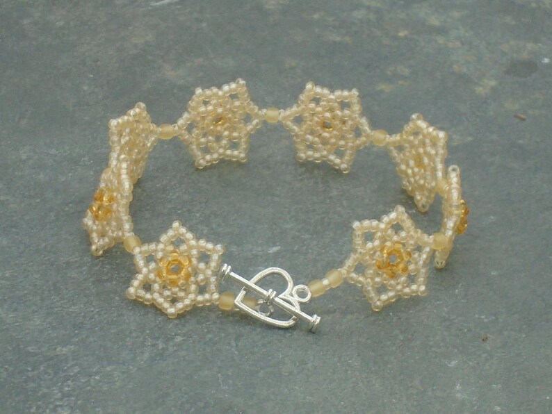 May include: A delicate bracelet made of white and gold beads, featuring a repeating flower design. The bracelet has a silver clasp.