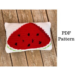 Pode incluir: Uma almofada retangular branca de crochê com uma grande fatia de melancia vermelha com detalhes de sementes pretas. A melancia tem uma casca verde. O texto "PDF Pattern" é visível.