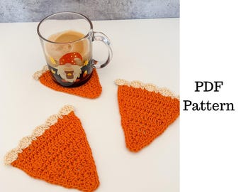 May include: Three orange crochet coasters shaped like pie slices with a beige scalloped edge. One coaster is under a clear glass mug with a gnome design. The text "PDF Pattern" is visible.