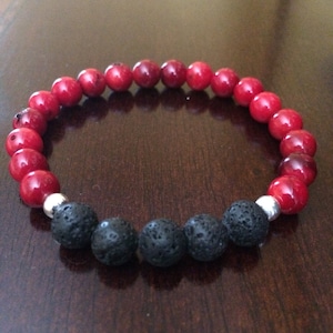 Puede incluir: Un brazalete de cuentas rojas y negras con detalles plateados. El brazalete está hecho con cuentas de coral rojo y cuentas de lava negra.