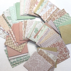 May include: A collection of square paper pieces with various patterns and colors. The designs include floral, geometric, and houndstooth patterns in shades of pink, green, beige, and brown. The papers are arranged in a semi-circular shape.