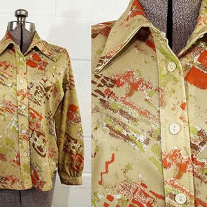 May include: A vintage button-down shirt with a tan background and an abstract pattern in shades of orange, brown, green, and white. The long-sleeved shirt has a collared neckline and is displayed on a mannequin.