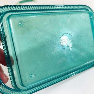 May include: A teal blue plastic tray with a raised edge and a scalloped border. The tray has a "PLASTIC" logo with the text "REG. TRADE MARK" above it.