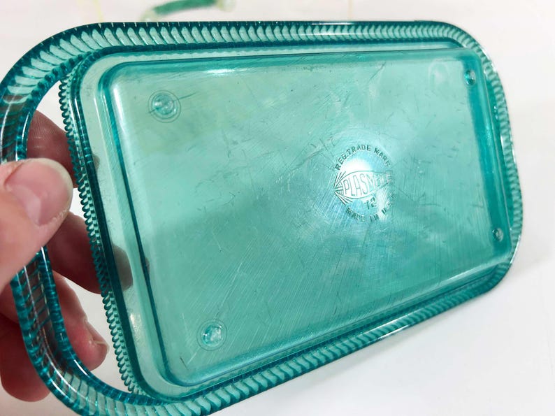 May include: A teal blue plastic tray with a raised edge and a scalloped border. The tray has a "PLASTIC" logo with the text "REG. TRADE MARK" above it.