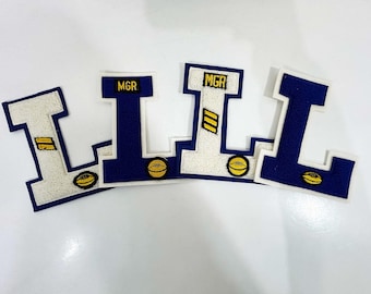 May include: Four embroidered letter patches in the shape of the letter "L". Each patch has a navy blue border and a white center. The top of each patch has the letters "MGR" in navy blue. Each patch has a football graphic.