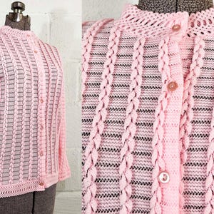 Könnte beinhalten: Ein rosa Häkelcardigan mit Knopfleiste und langen Ärmeln. Der Cardigan hat ein zartes, durchbrochenes Muster.