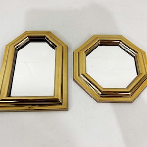 May include: Two wall mirrors with polished gold-tone frames. One mirror features an arched top design, while the other is octagonal in shape. Both mirrors have reflective glass surfaces surrounded by thick, smooth, metallic-finished borders.