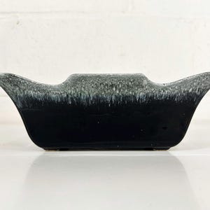 Puede incluir: Un macetero de cerámica esmaltada en blanco y negro con un diseño ondulado único. El macetero tiene una forma ancha y poco profunda y un acabado liso y brillante.