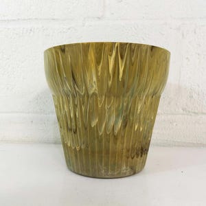 May include: A green and yellow ceramic planter with a wavy, marbled design. The planter has a wide, round opening and a slightly tapered base.