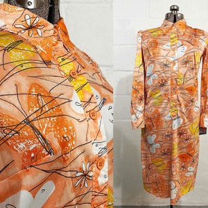 May include: A long-sleeve shirt dress in a peach-orange hue featuring a repeating pattern of white, yellow, and orange butterflies and stylized flowers. The garment includes a pointed collar, a front button placket with orange buttons, and cuffs.