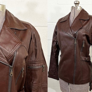 May include: A brown leather jacket with a classic biker style. The jacket features a notched collar, a diagonal zipper closure, and multiple zippered pockets. The sleeves have zippered details and the jacket is displayed on a mannequin.