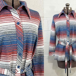 May include: A vintage button-down shirt with a striped pattern in red, white, blue, and gray. The long-sleeved shirt features a collar, a matching belt, and is displayed on a mannequin. The shirt has a retro style.