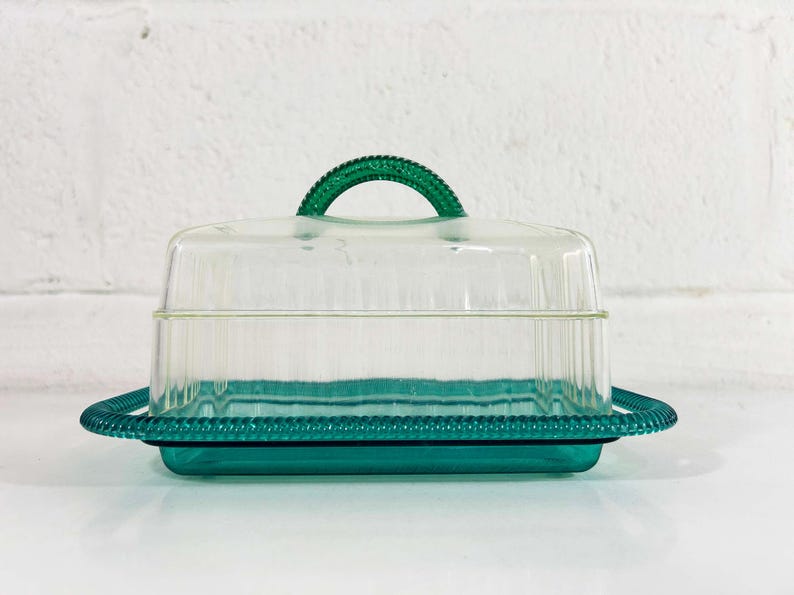 May include: A clear glass butter dish with a green lid and base. The lid has a green handle.