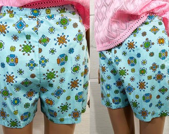 May include: Pale blue shorts patterned with colourful geometric shapes in orange, green, and blue. The shorts have a high waist and a relaxed fit, ideal for a retro or vintage style.
