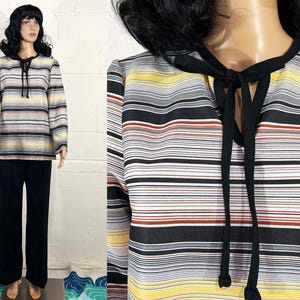 May include: A vintage striped top and black pants set. The long-sleeved top features horizontal stripes in shades of gray, yellow, and brown, with a black tie at the neckline. The pants are solid black and have a wide-leg design.