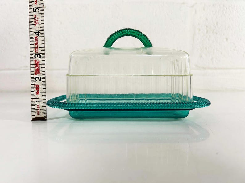 May include: A clear plastic butter dish with a green lid and base. The lid has a handle and the base has a decorative edge.