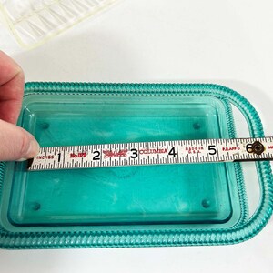 May include: A teal blue glass dish with a raised rim and a beaded edge. The dish is 5 inches long and is being measured with a ruler.