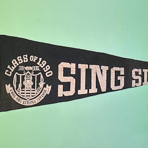 May include: Black felt pennant with white text that reads "Class of 1990 Sing Sing" and a graphic of a person behind bars with the text "The 30/30 Club Bars and Stripes Forever".