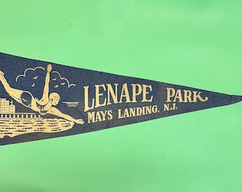 May include: A blue pennant with a white border and gold lettering. The pennant features a woman diving into water with a cityscape in the background. The text reads "Lenape Park Mays Landing, N.J."