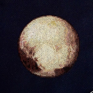 May include: A cross-stitch embroidery of Pluto, a dwarf planet in our solar system, on a dark blue fabric. The embroidery is detailed and shows the planet's surface features.