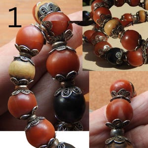 May include: A close-up of a red and black beaded bracelet with silver filigree accents. The bracelet is made of round beads with a variety of textures and finishes. The beads are strung on a cord and secured with a clasp.