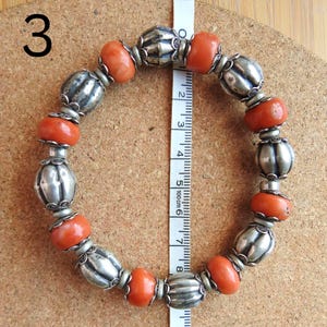 May include: A bracelet made of orange coral and silver beads. The bracelet is approximately 6 inches in length.