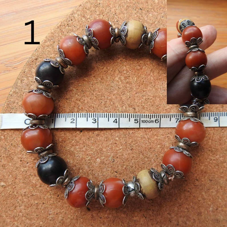 May include: A bracelet made of brown, black, and white beads with silver wire accents. The bracelet measures approximately 6 inches in length.