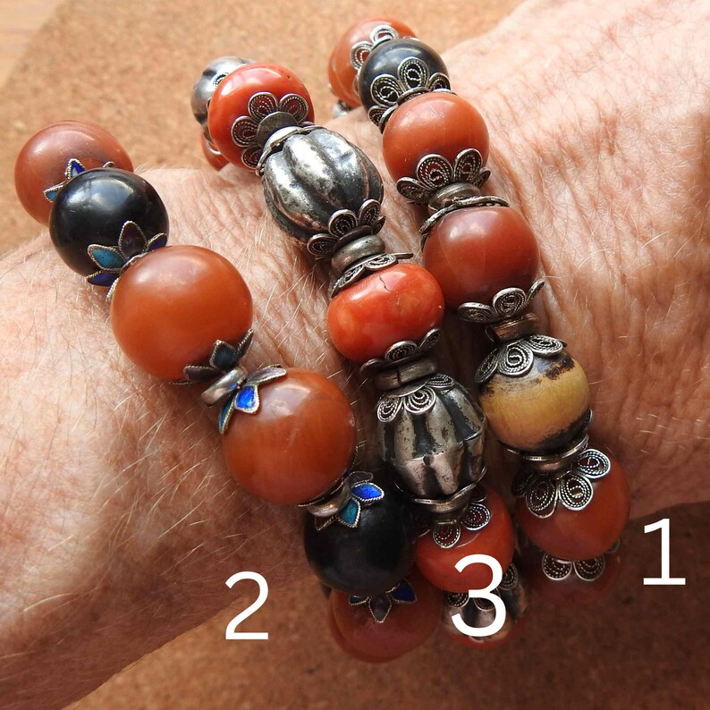 May include: Three beaded bracelets with amber, coral, and bone beads. The bracelets are adorned with silver filigree and blue enamel accents. The bracelets are numbered 1, 2, and 3.