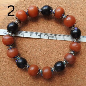 May include: A bracelet made of brown and black beads with silver accents. The bracelet is approximately 6 inches in length.