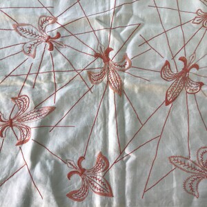 May include: White fabric with a red embroidered pattern of stylized flowers. The flowers are arranged in a repeating pattern across the fabric.