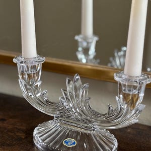 Puede incluir: Un candelero de cristal transparente con un diseño decorativo en espiral. El candelero tiene dos brazos y una base redonda. Está etiquetado como "Bohemia" en la parte inferior.