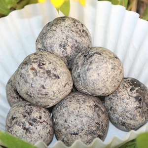 May include: A group of six round, dark gray and light gray speckled stones in a white paper cup.