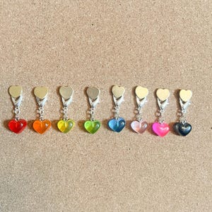 May include: Nine heart-shaped charms with different colored resin inserts. The charms are attached to silver-toned metal rings.