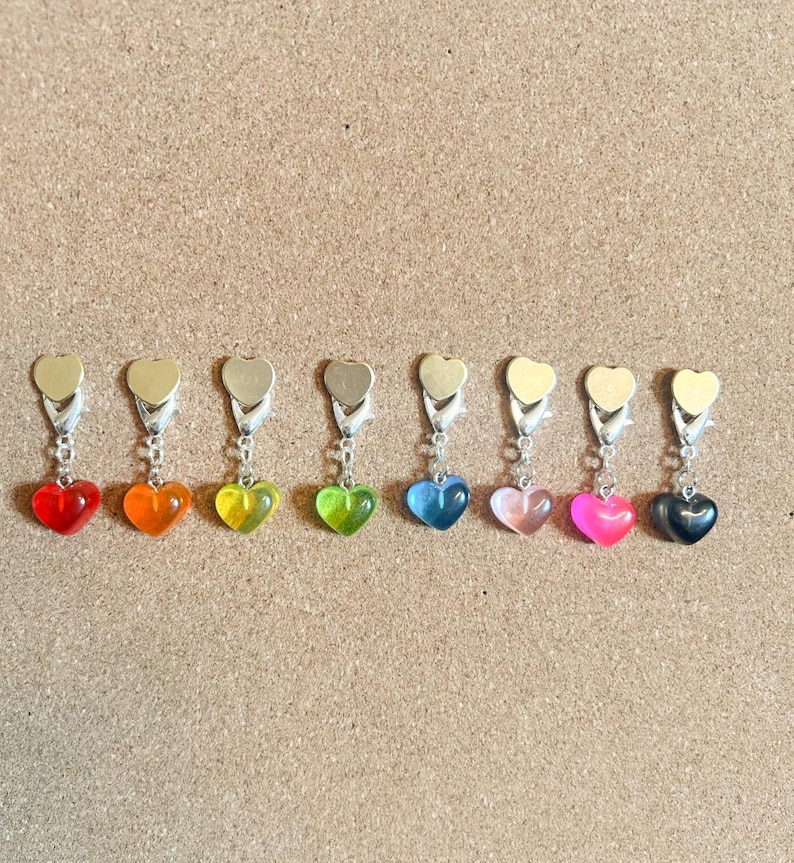 May include: Nine heart-shaped charms with different colored resin inserts. The charms are attached to silver-toned metal rings.
