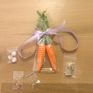 May include: Two orange and white carrot-shaped decorations tied together with a purple ribbon and packaged in a clear plastic bag.  There are four small bags with various small items, including a pair of earrings, a charm, and a key chain with a horseshoe charm.  The bags have the text "Thank You" printed on them.