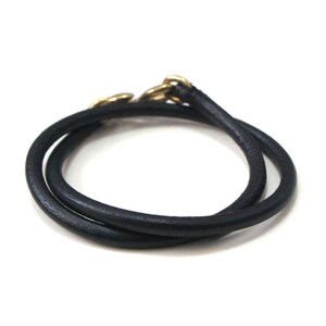 Puede incluir: Un brazalete de cuero negro con un cierre dorado.